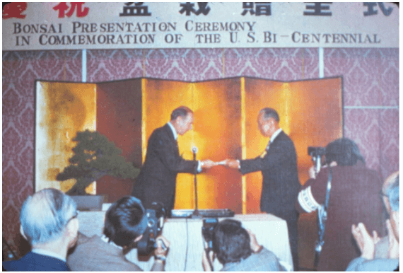 Nobusuke Kishi, cựu chủ tịch Hiệp hội Bonsai Nippon, trao danh sách 53 cây Bonsai cho Đại sứ Hoa Kỳ James Hodgson tại một buổi lễ ở Tokyo, Nhật Bản. Cây bên trái là cây thông Đen Nhật Bản đầu tiên của Nhật Bản tặng cho Bảo tàng.